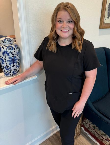 A woman in a black scrub top is standing next to a blue chair.