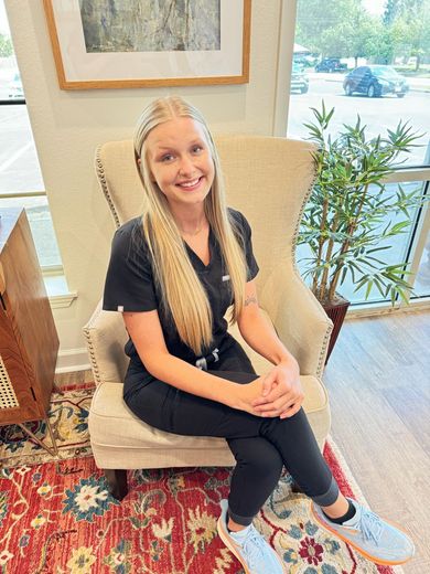 A woman is sitting in a chair with her legs crossed and smiling.