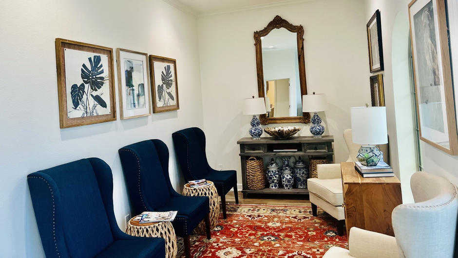 A waiting room with blue chairs , a couch , a mirror and a rug.