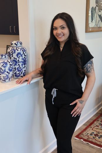 A woman in a black scrub top and black pants is standing next to a counter.