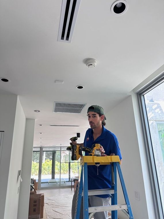 A man is standing on a ladder in a room holding a drill.
