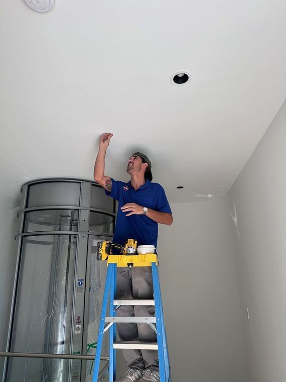 A man is standing on a ladder working on a ceiling.