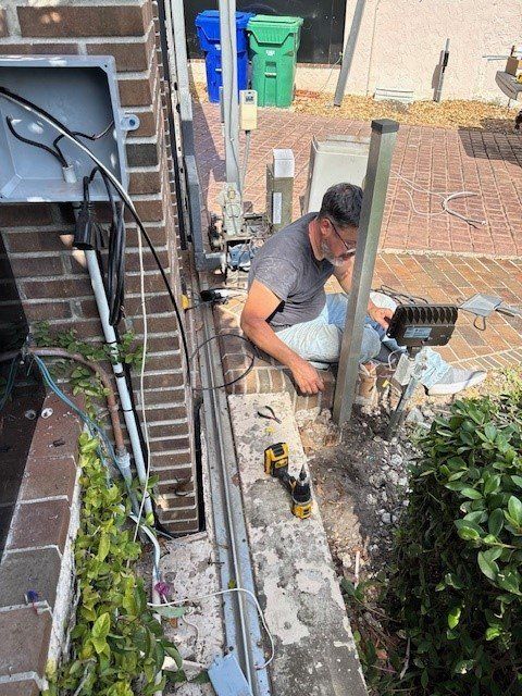 A man is sitting on a brick wall working on a fence.