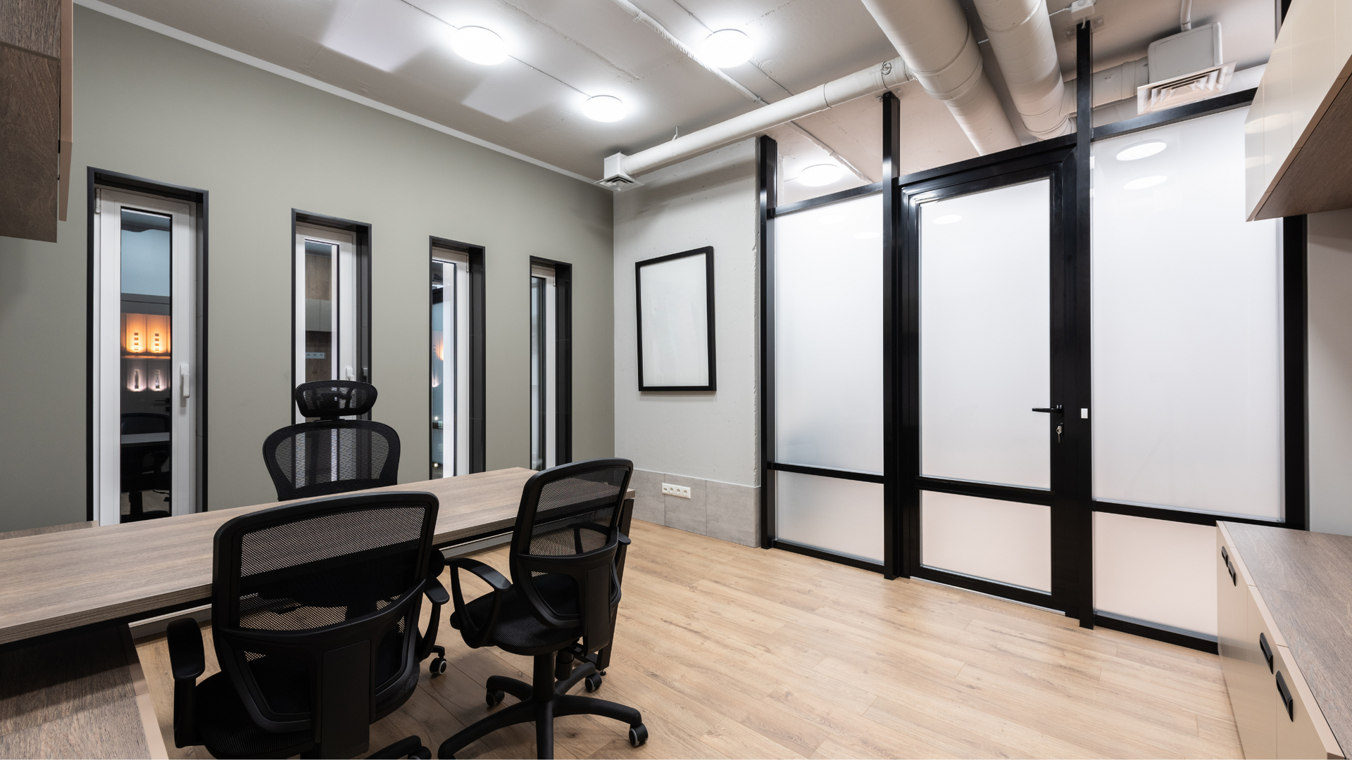 Modern office with neutral walls, wood flooring, and frosted glass partitions.