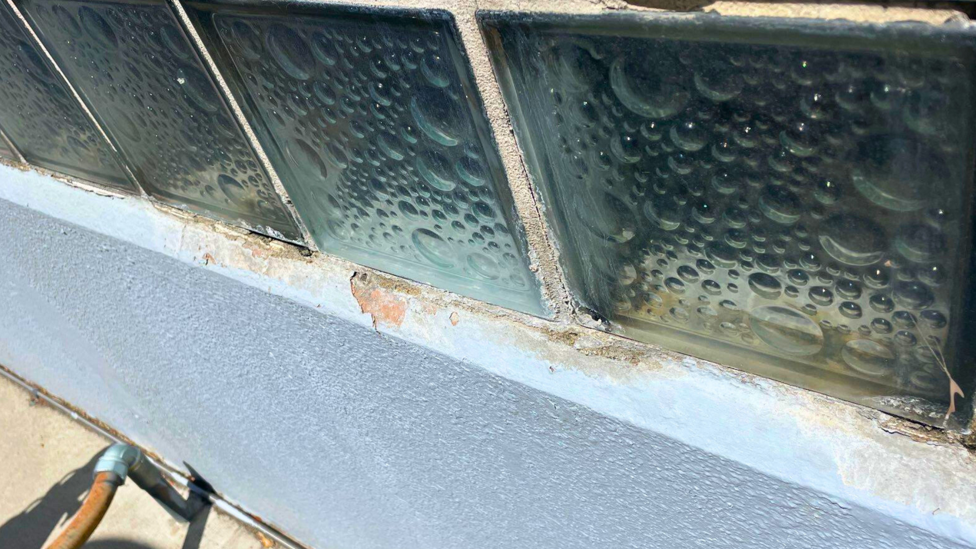 Close-up of damaged commercial building exterior with peeling paint and exposed brick beneath glass 