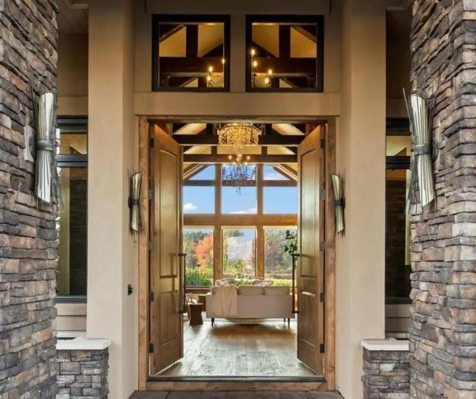 The front door of a house is open to a living room with a chandelier hanging from the ceiling.