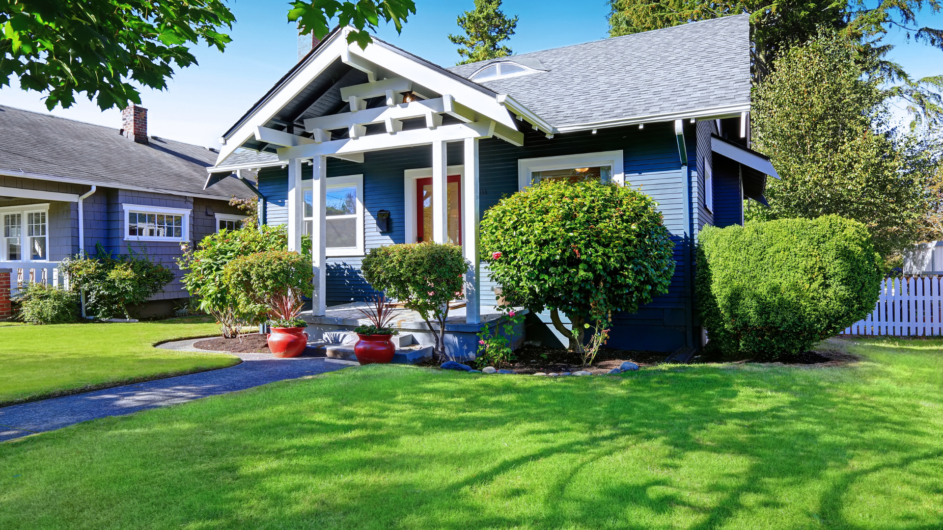 A blue house with a white porch and a lush green lawn in front of it.