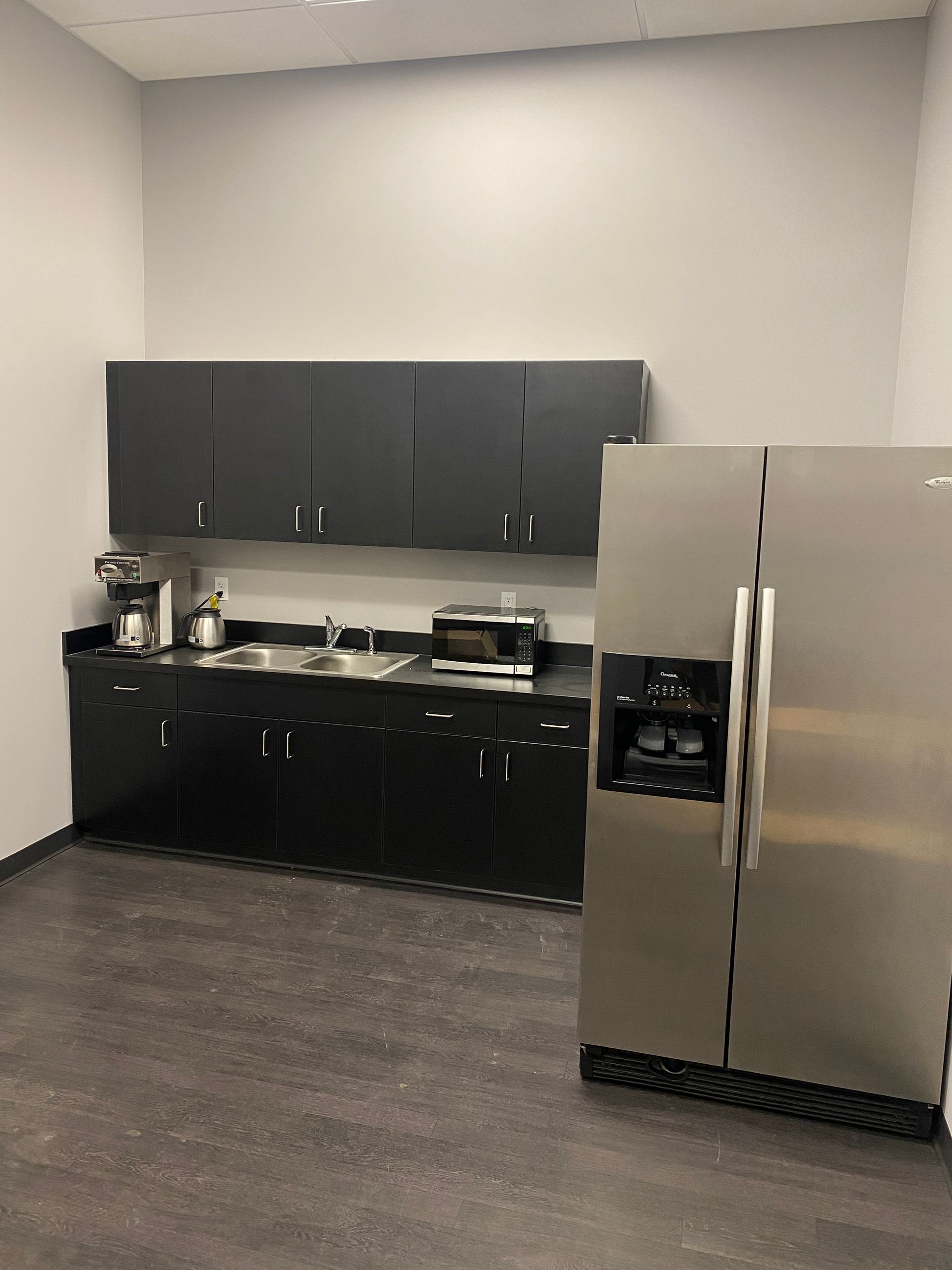 A kitchen with black cabinets and a stainless steel refrigerator