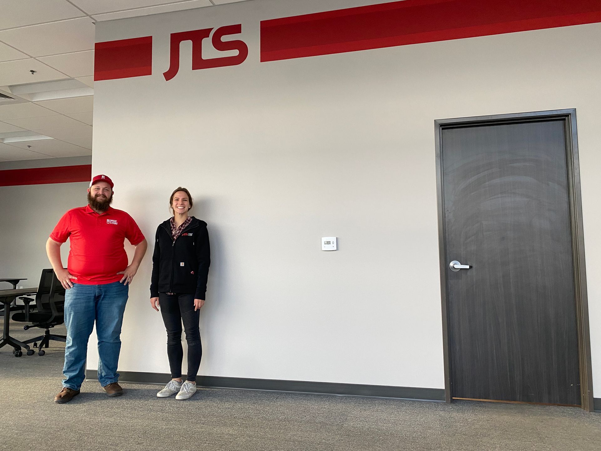 A man and a woman are standing in front of a wall with the word jts on it.