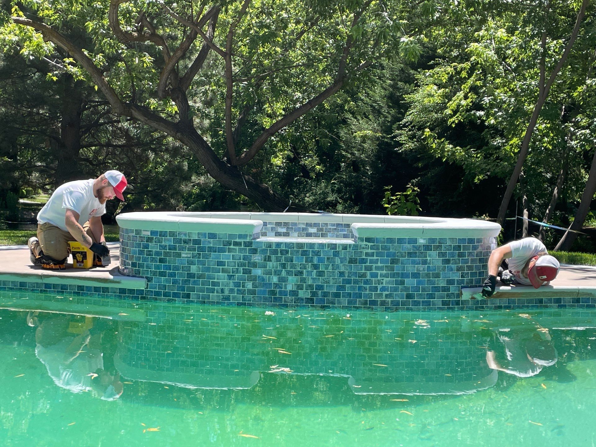 Two men are working on the side of a swimming pool.