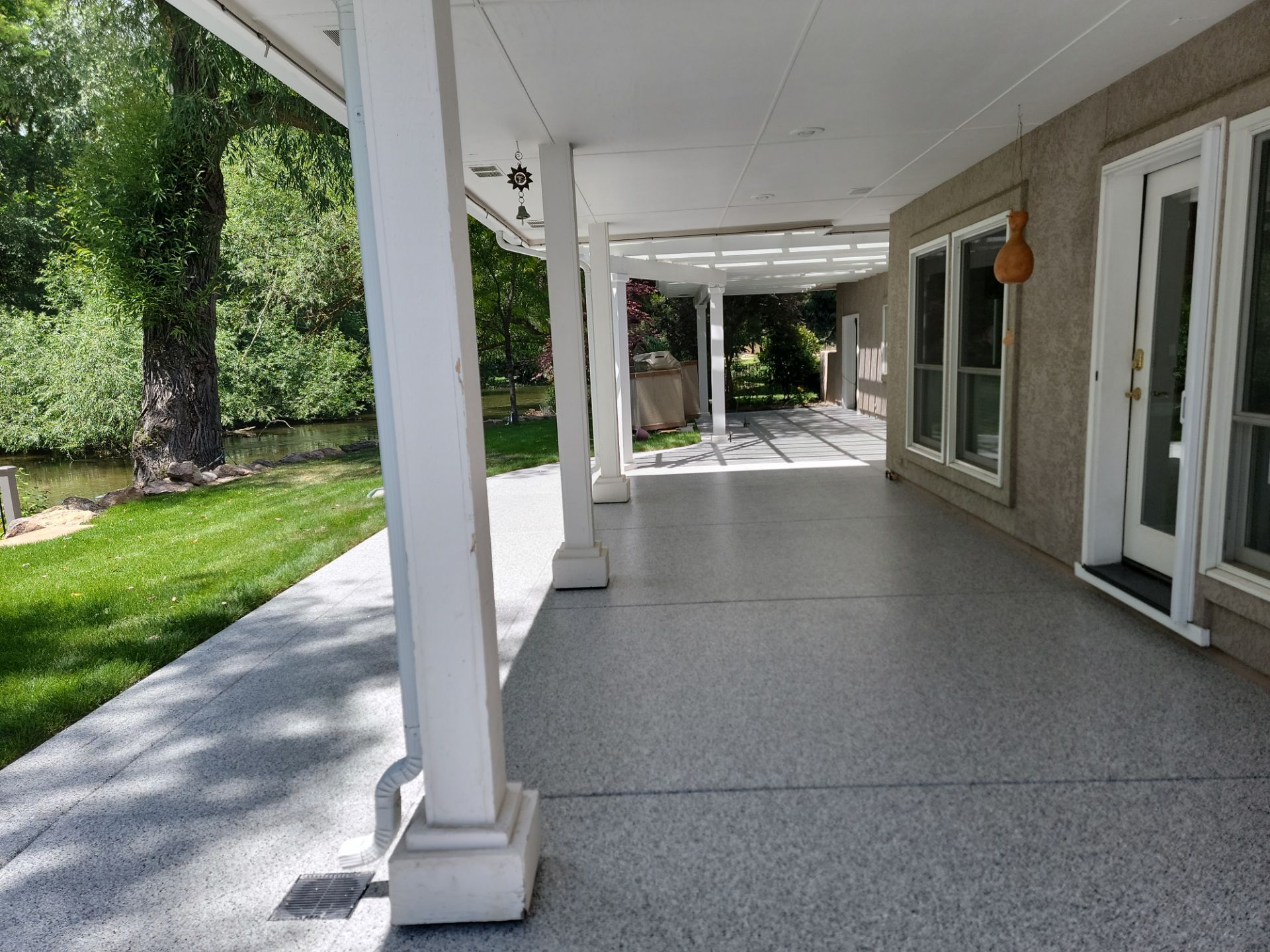 A large porch with a gray concrete floor and white pillars
