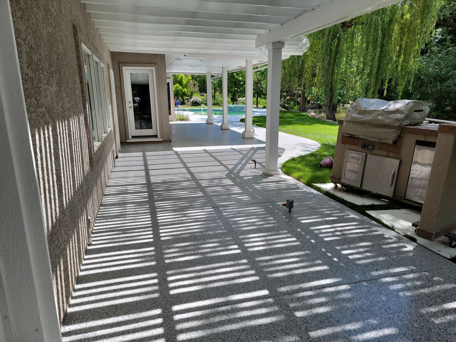 A patio with a pergola and a grill in the backyard of a house.