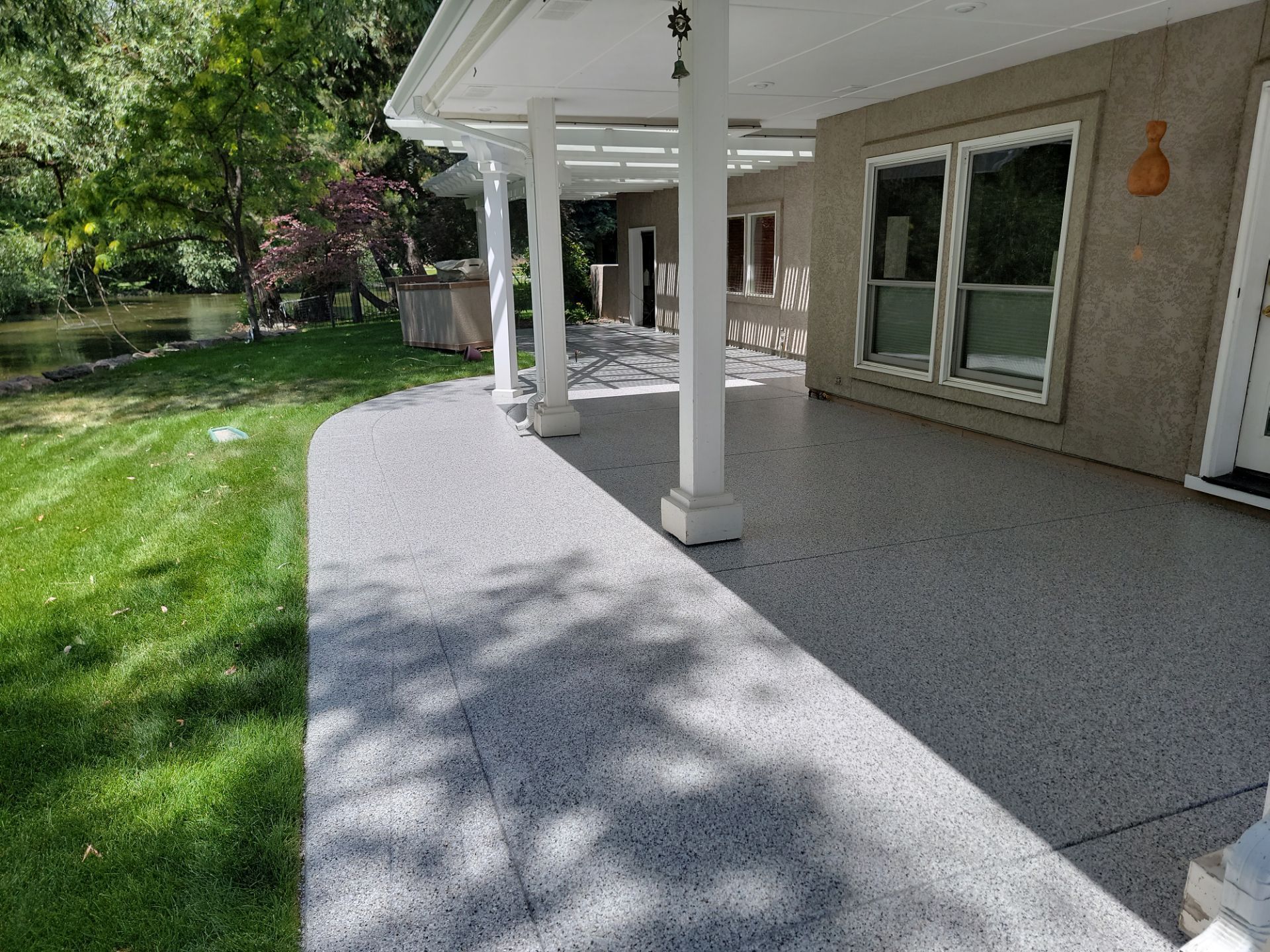 A patio with a pergola and a concrete floor in front of a house.
