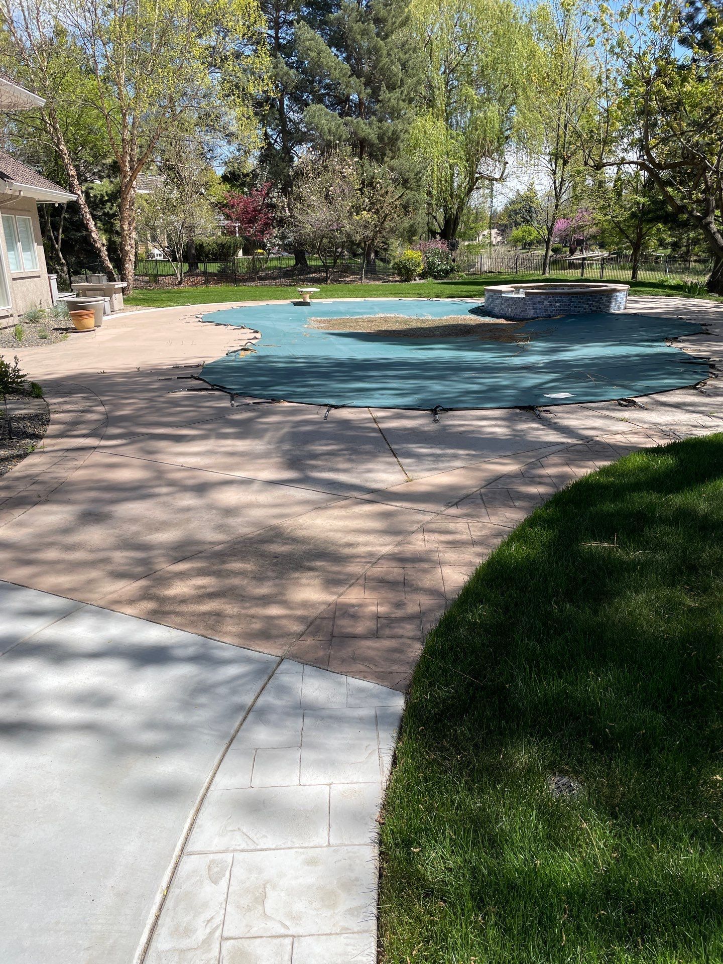A swimming pool with a blue cover on it is surrounded by trees and grass.