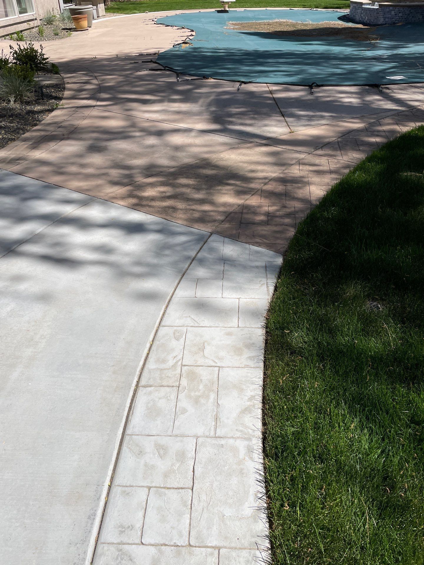 A concrete walkway leading to a pool with a blue cover on it.