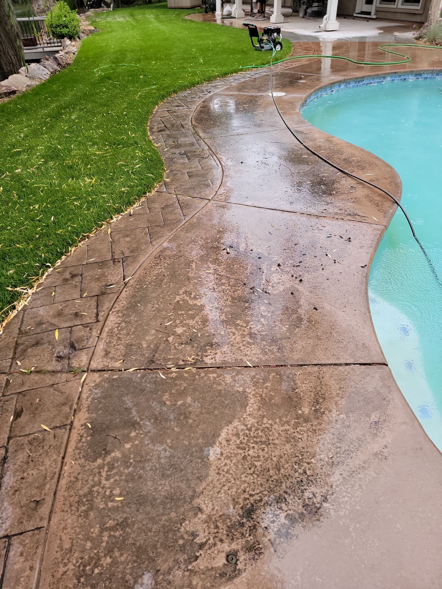 A concrete walkway next to a swimming pool in a backyard.