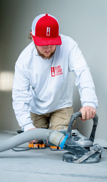 A man in a red hat is using a grinder on a concrete floor.