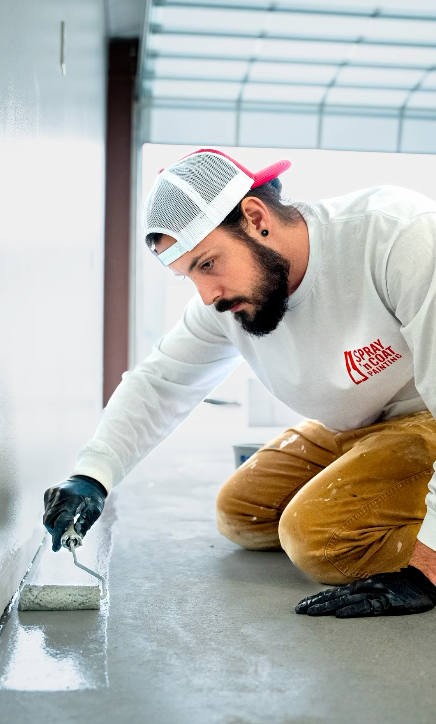 A man is kneeling down and painting the floor with a roller.