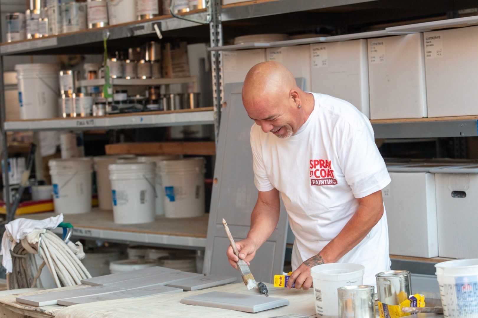 A man in a white shirt is painting a piece of wood.