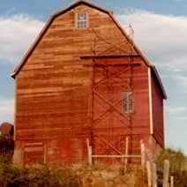 A large red barn is sitting in the middle of a field.