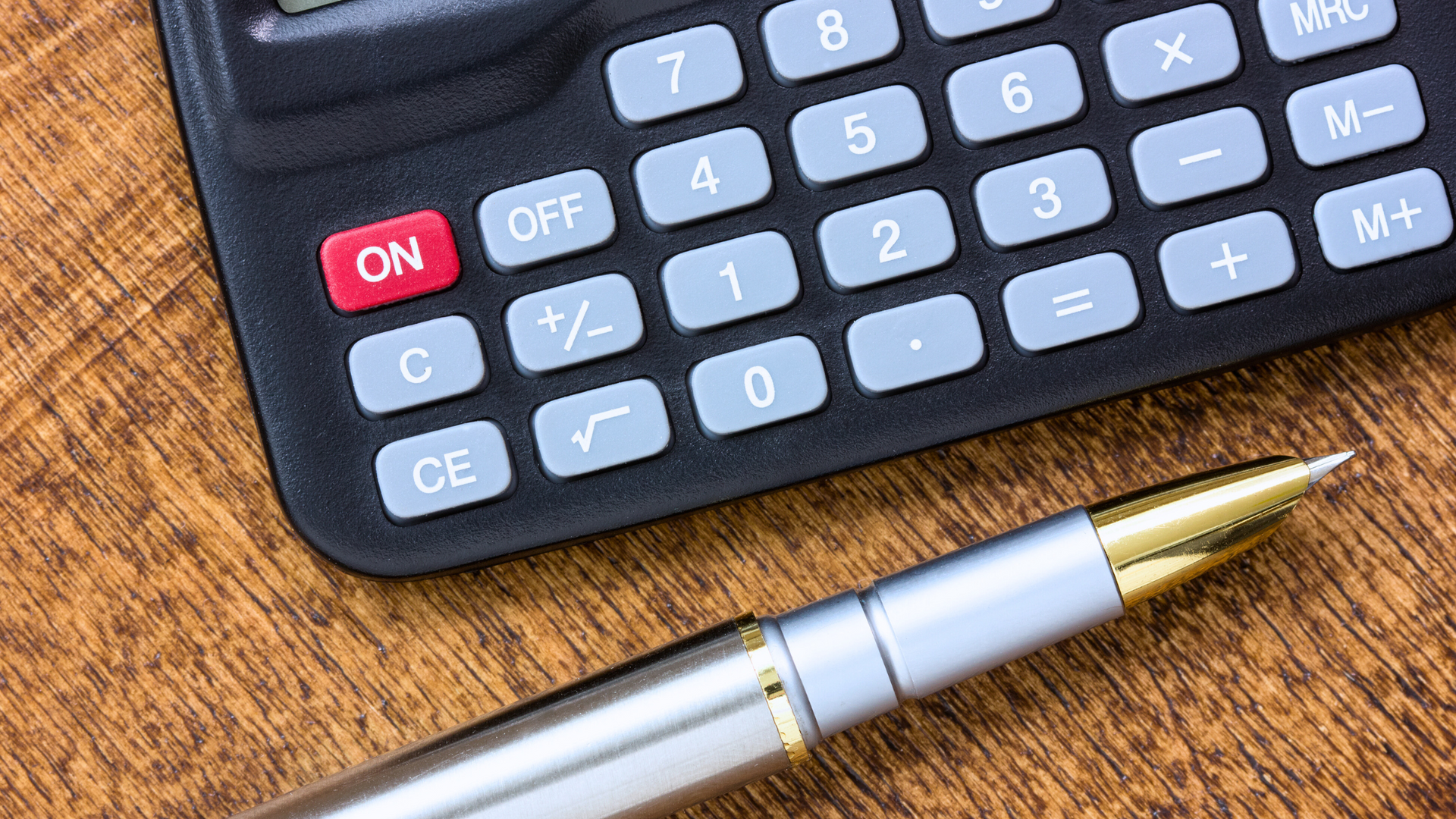 A pen is sitting next to a calculator on a wooden table.