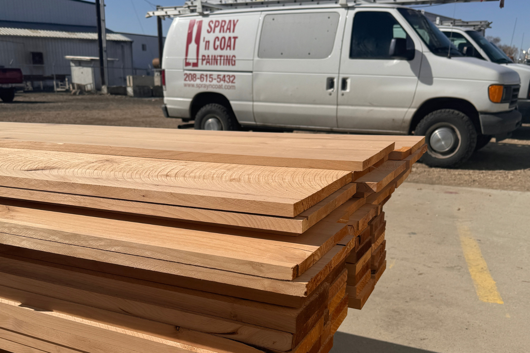A white van is parked next to a stack of wood.
