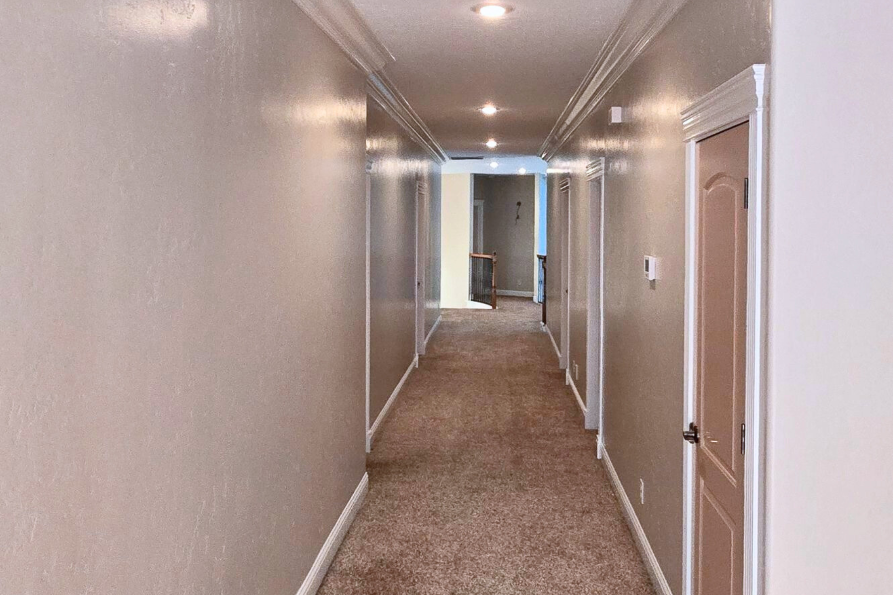 A long hallway with a brown carpet and white walls.