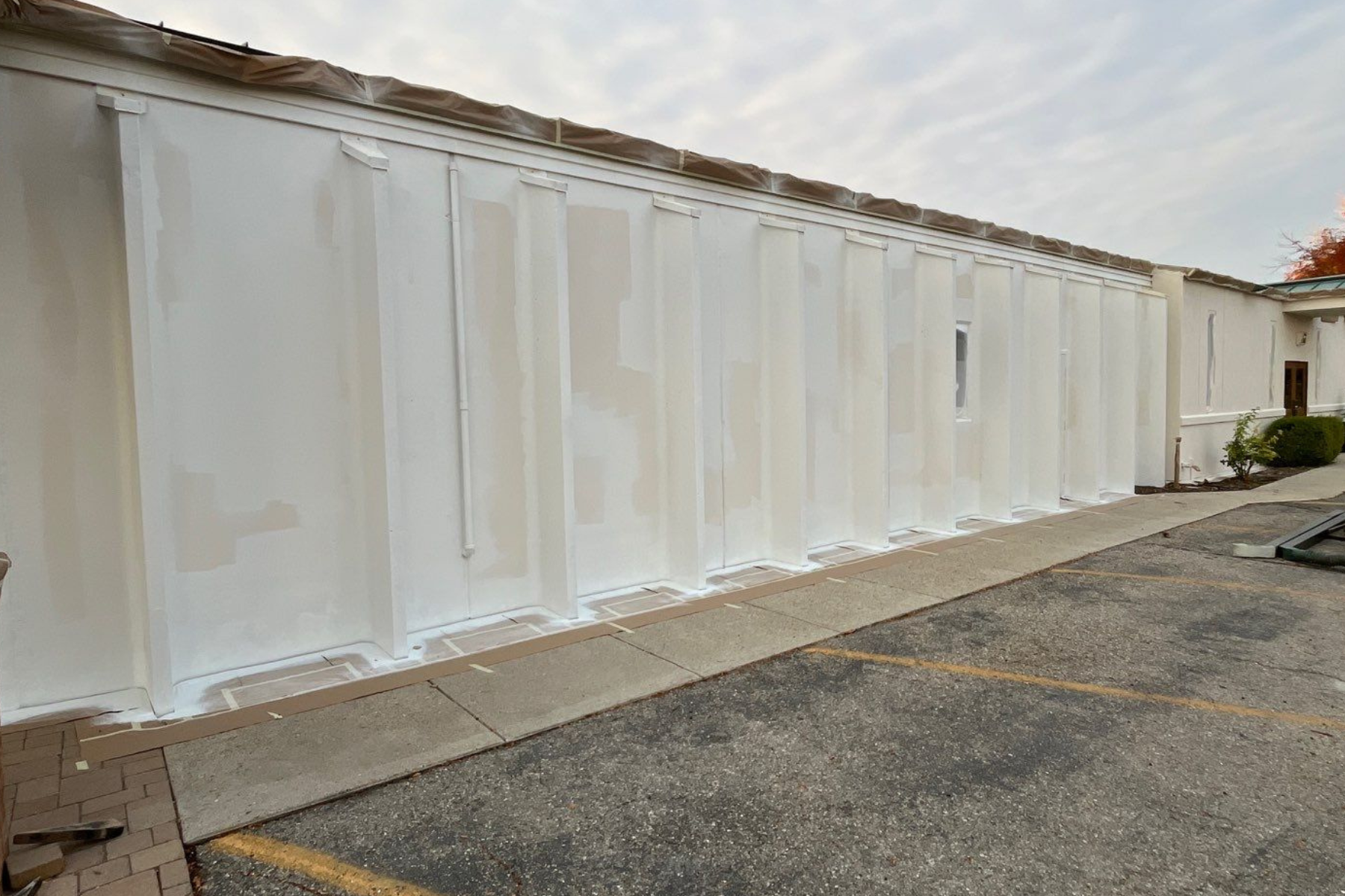 A large white wall is being painted in a parking lot.
