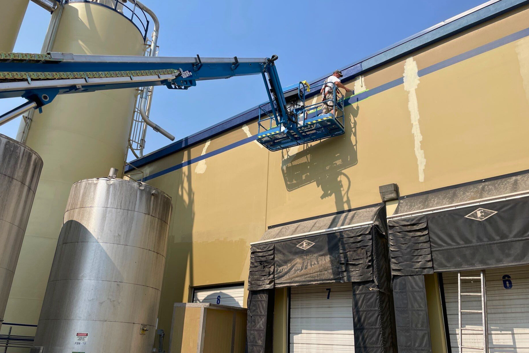 A man is painting the side of a building with a crane.