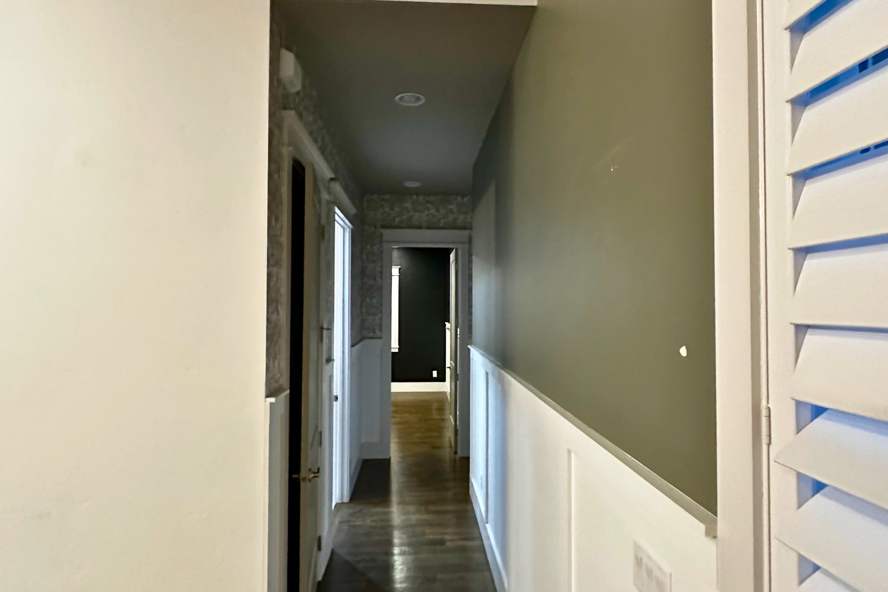 A long hallway with shutters on the walls and a door.