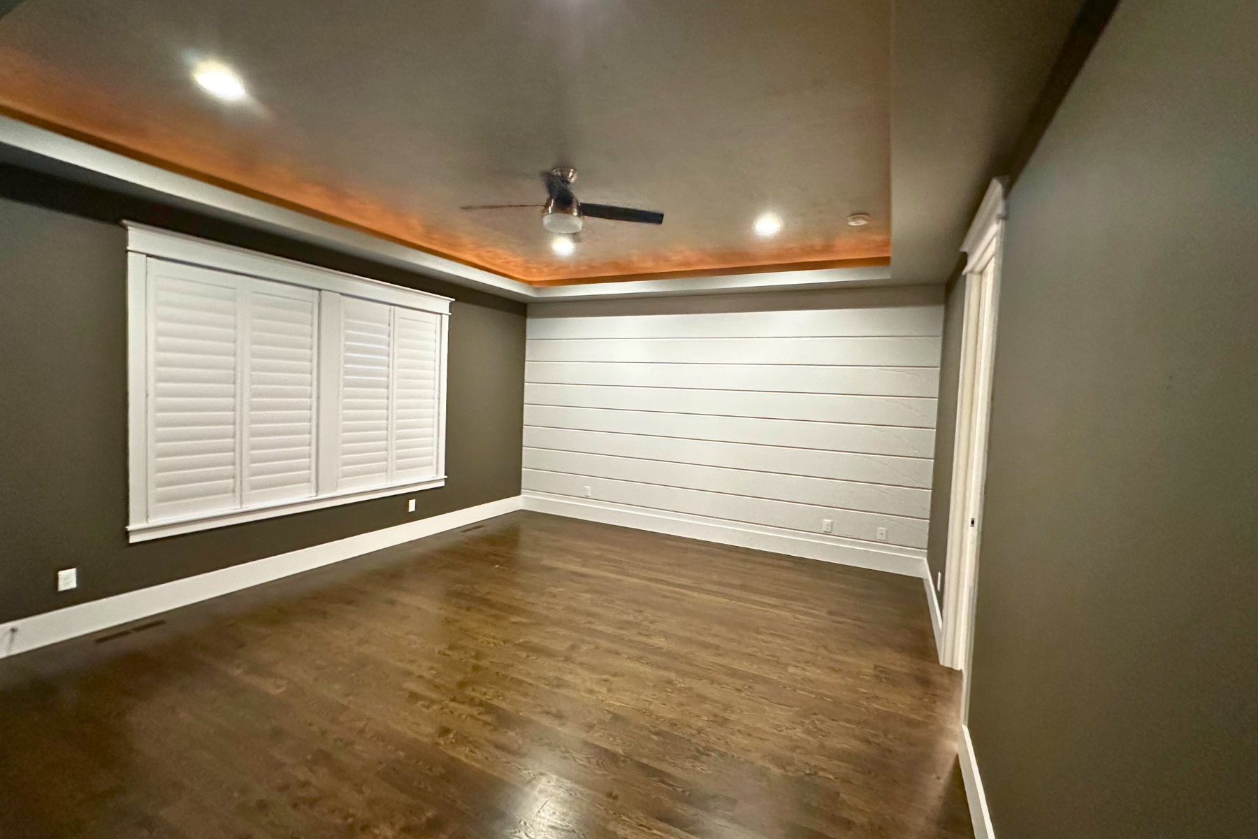 A large empty room with hardwood floors and a ceiling fan.