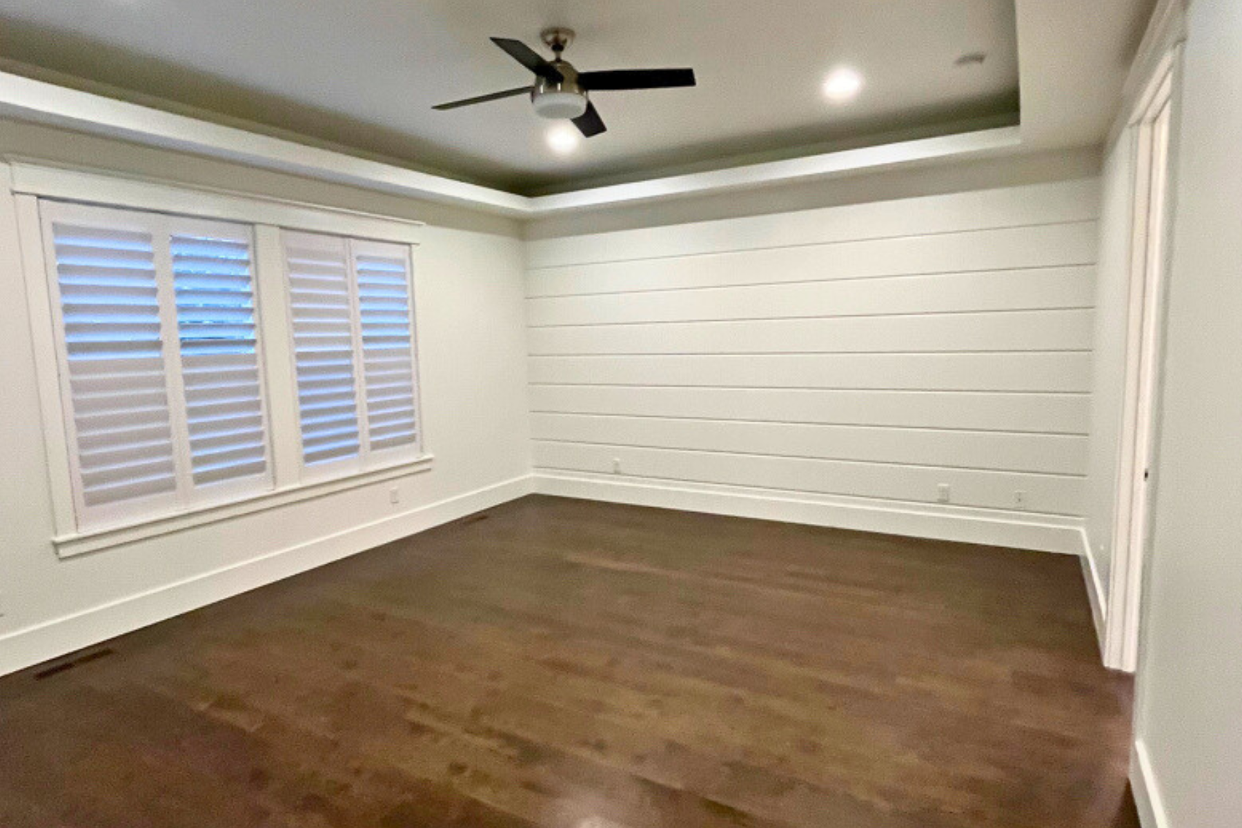 An empty room with a ceiling fan and shutters on the windows.