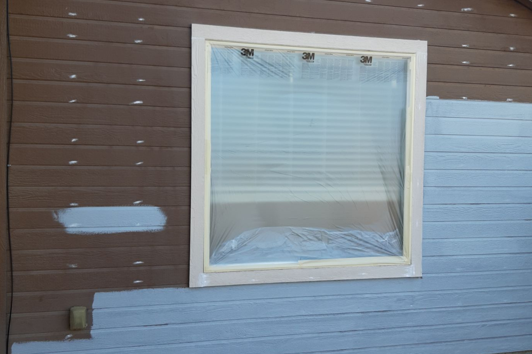 A window is being painted on the side of a house
