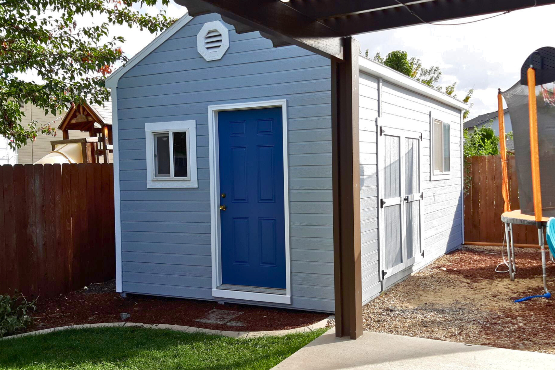 A blue and white shed with a blue door in a backyard.