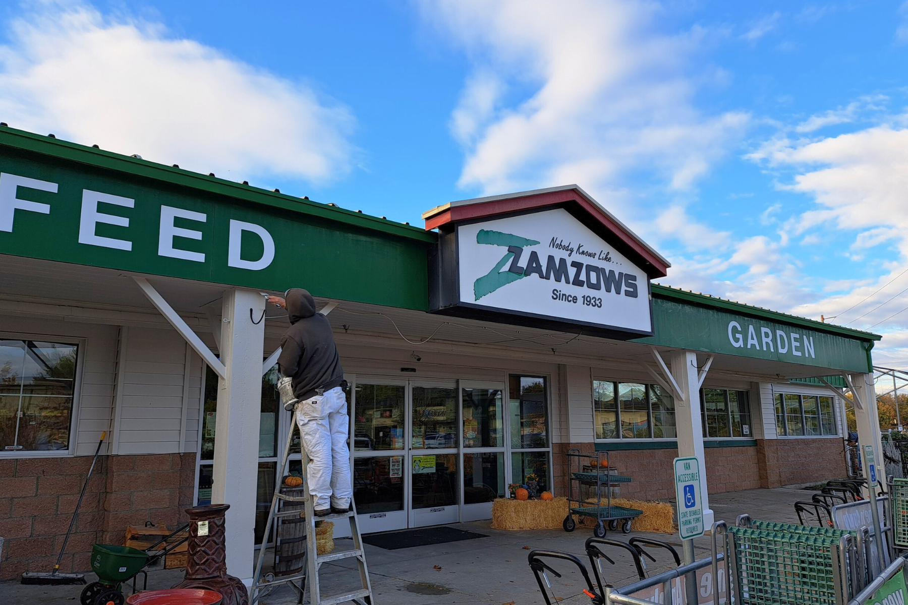 A man is standing on a ladder in front of a feed store.