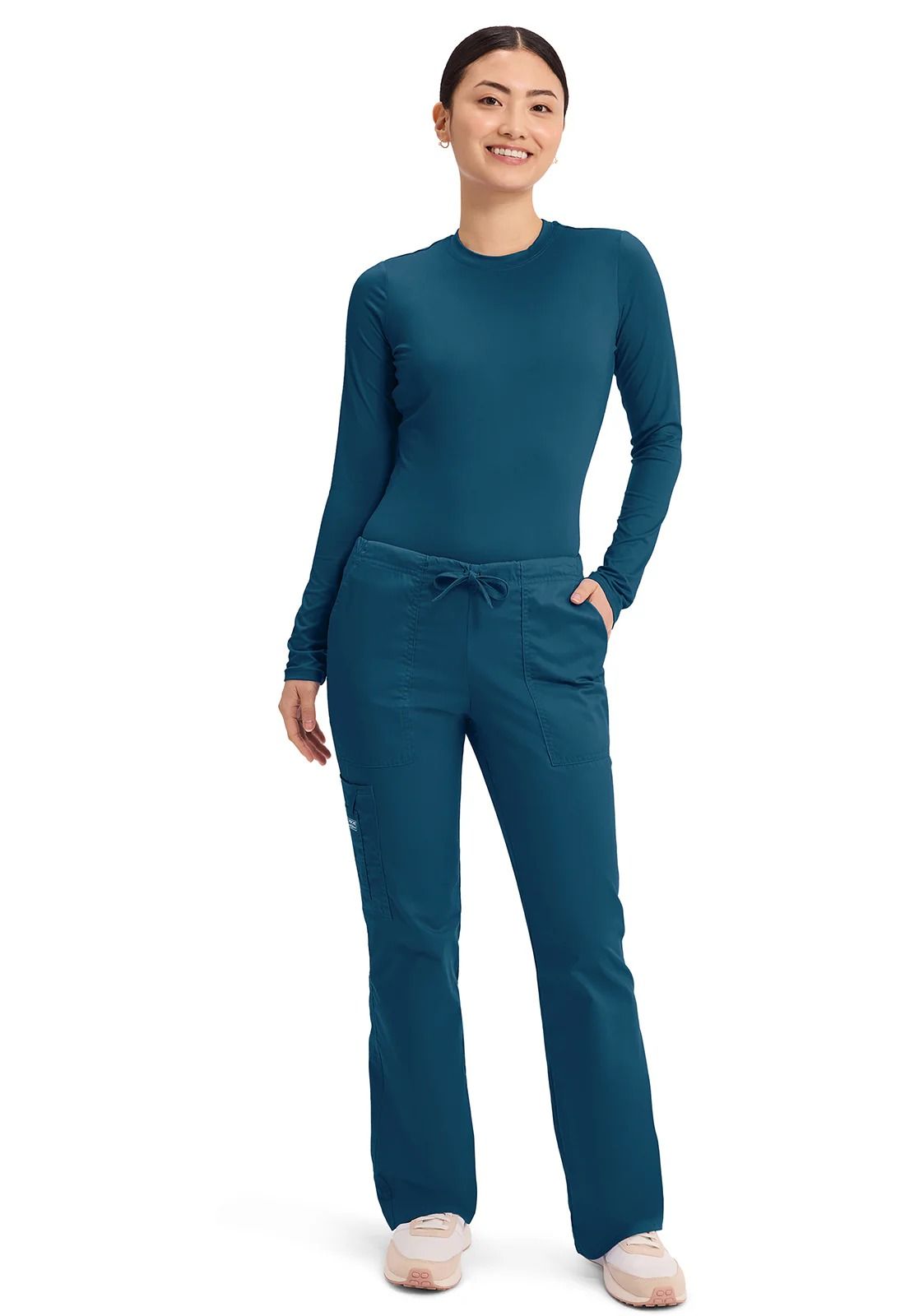 Woman in teal scrubs smiles, hands in pockets.