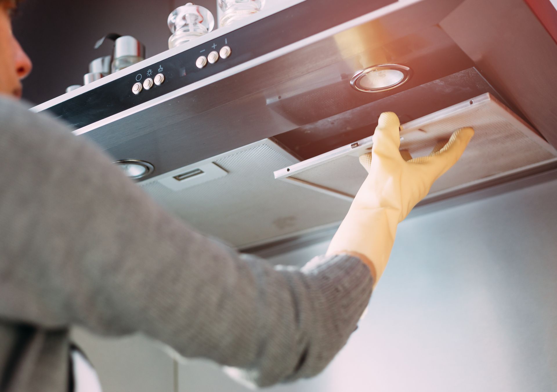 Person wearing a glove removing a dirty range hood filter in a kitchen.