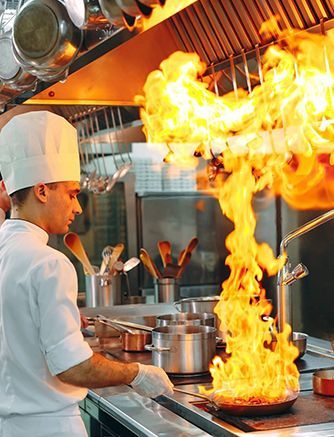 A chef is cooking in a kitchen with flames coming out of a pan.
