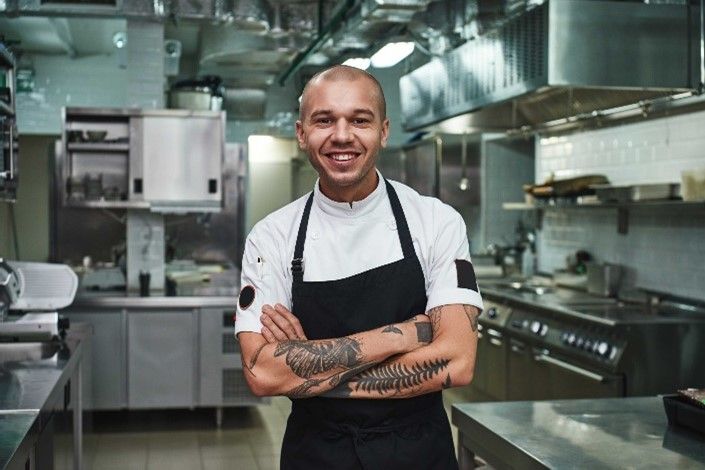 A chef is standing in a kitchen with his arms crossed and smiling. A chef is standing in a kitchen with his arms crossed and smiling.