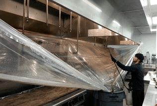 A man is cleaning a kitchen hood with a plastic bag.