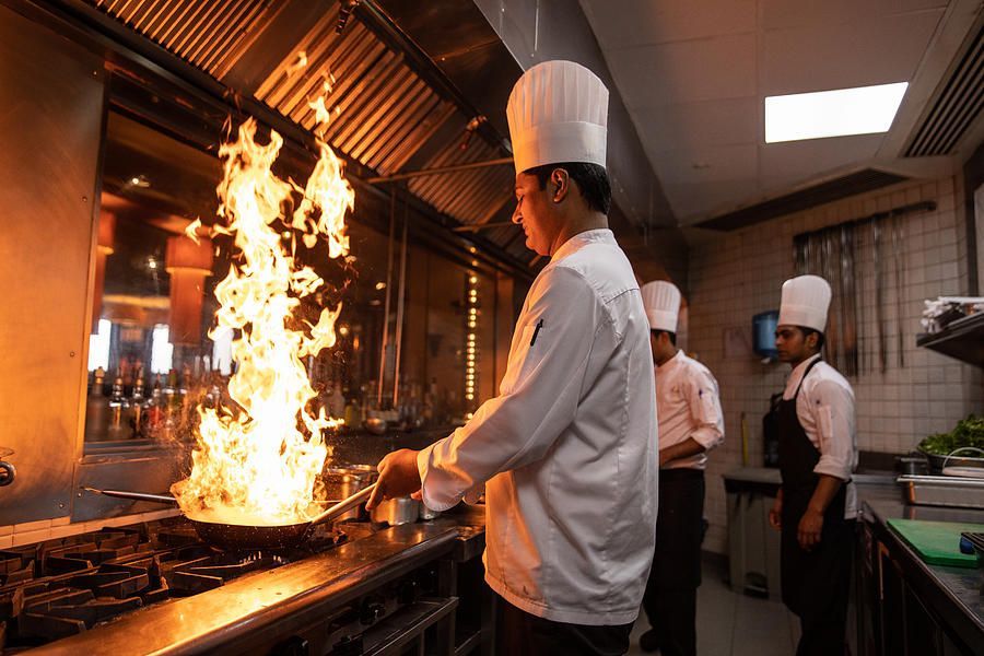 A chef is cooking food in a kitchen with flames coming out of a pan.