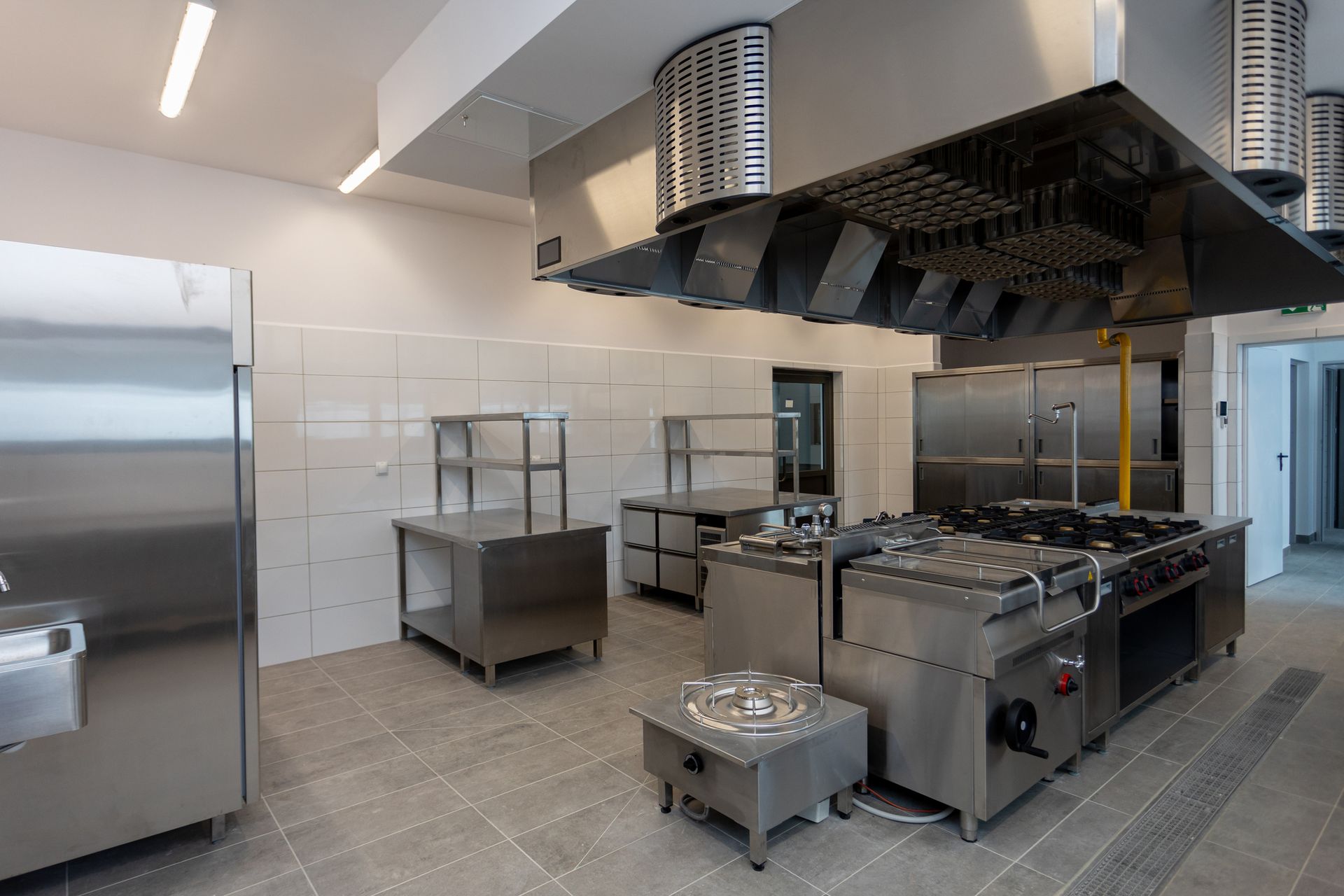 Commercial kitchen hood in a spacious, modern kitchen with stainless steel appliances.
