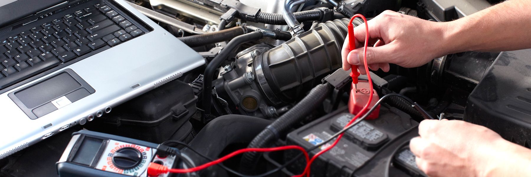 A person is working on a car with a laptop in the background.