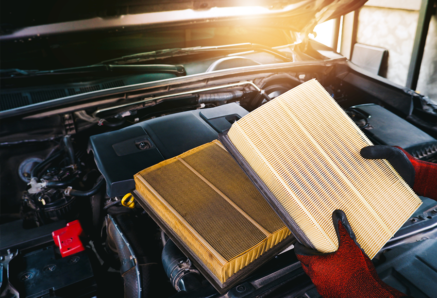 a person wearing gloves is holding an air filter in front of a car engine