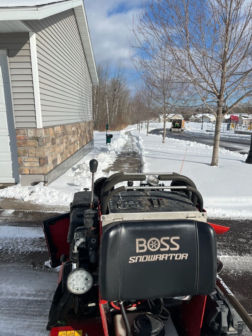 A boss snow blower is parked in front of a house in the snow.