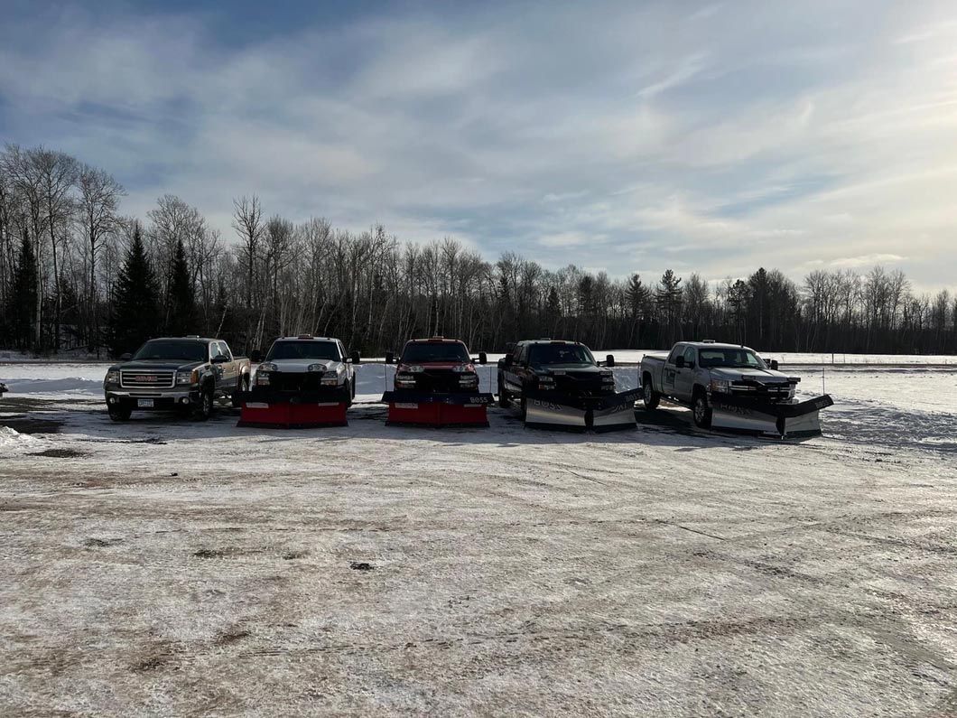 A row of snow plows are parked in a snowy field.