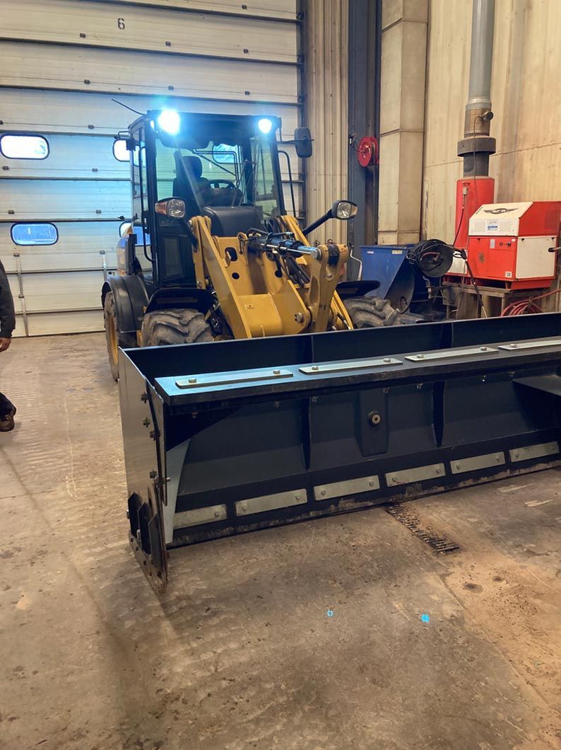 A yellow tractor with a large bucket is parked in a garage.