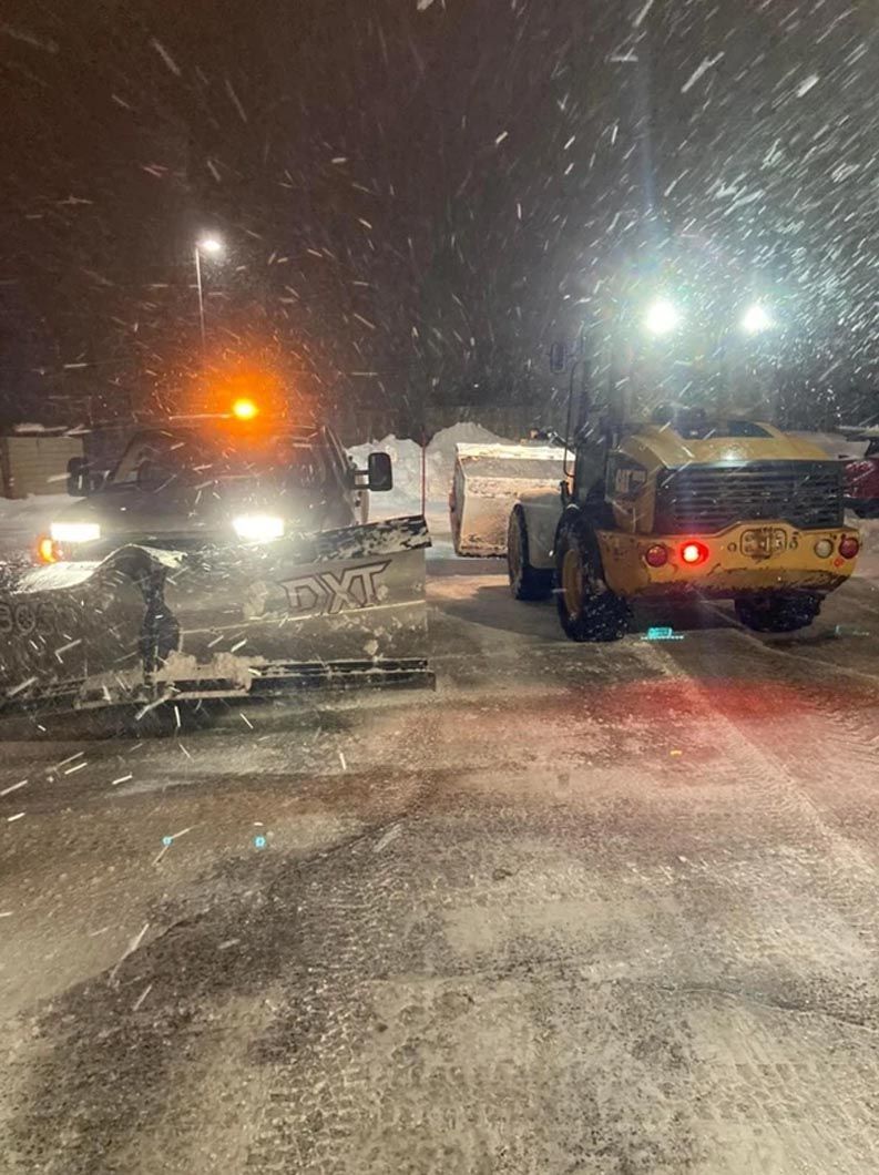 A snow plow is plowing a parking lot at night.