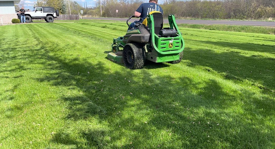 A man is riding a lawn mower on a lush green lawn.