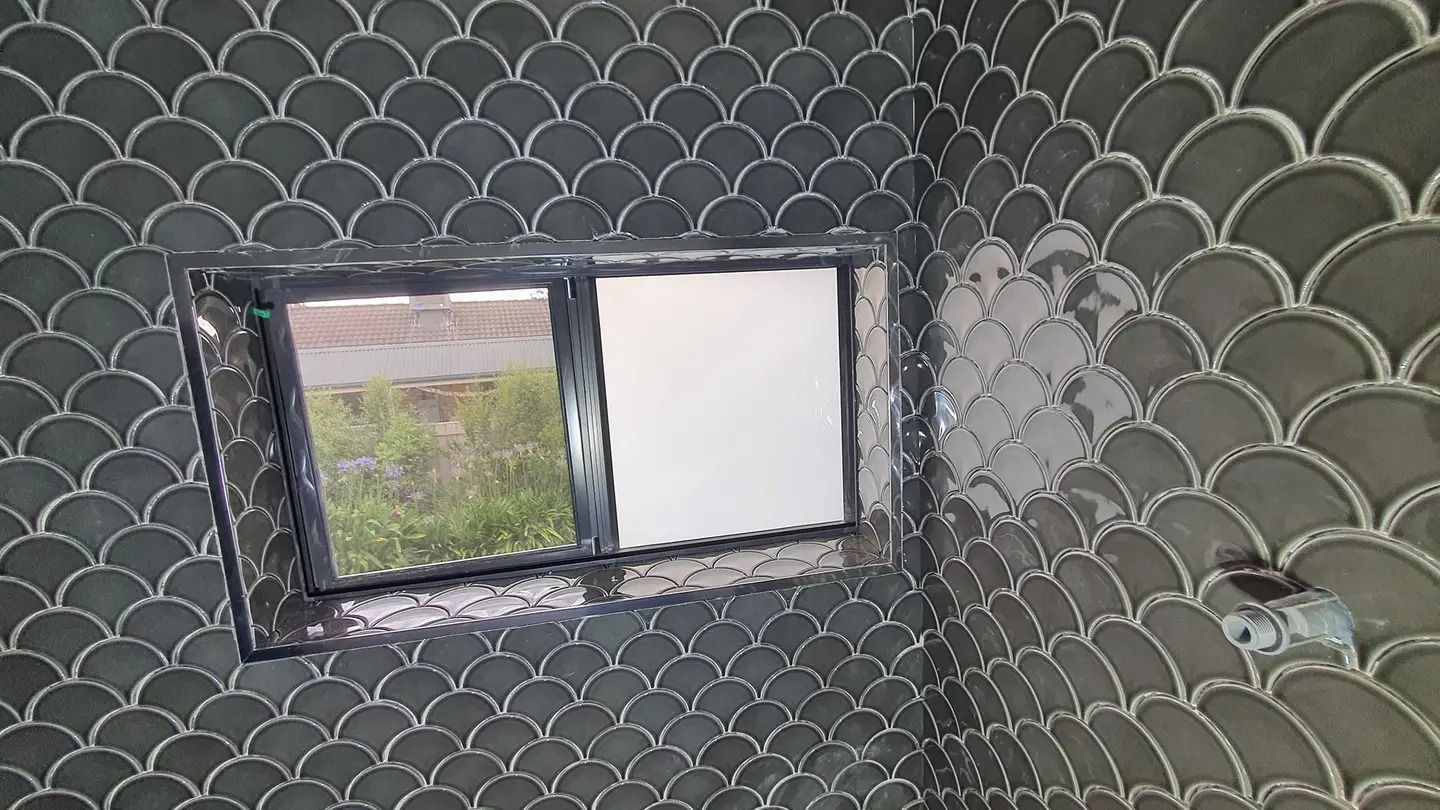 Dark grey scale-shaped tile in a corner of a room, window with black frame, outdoor view — David Son Tiling in Springdale Heights, NSW